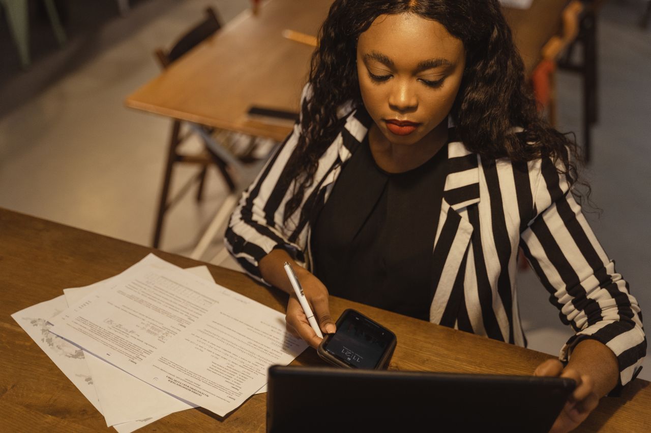 A supervisor checks her phone at a desk, papers beside her